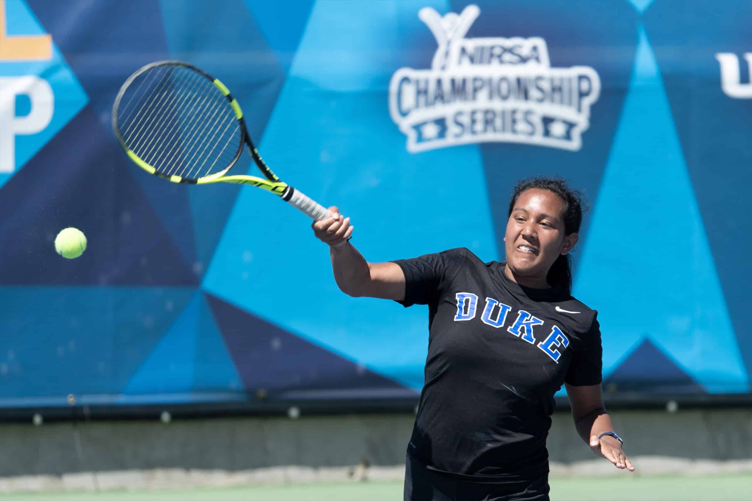 Young woman wearing a DUKE shirt swinging a tennis racquet