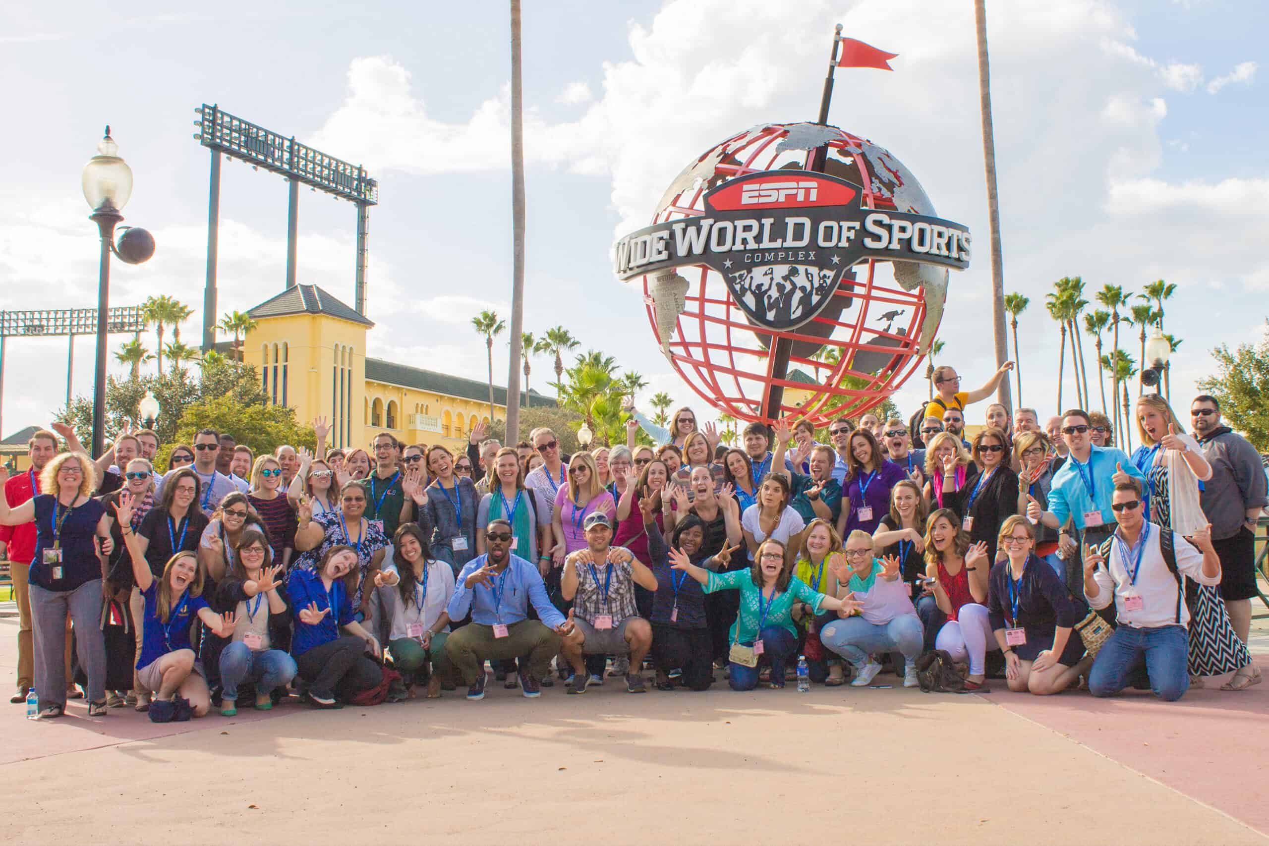 A large, smiling group poses in front of the ESPN Wide World of Sports globe on a sunny day.