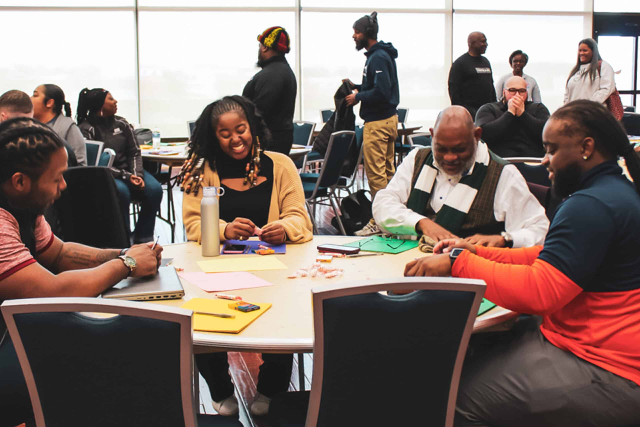 People sitting around tables in a room, smiling and working together on a group activity during a meeting.