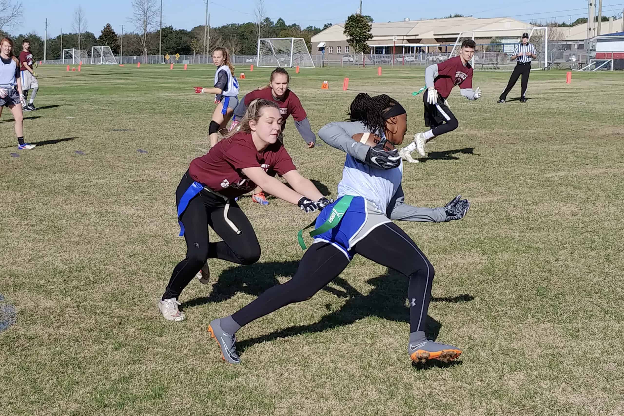 Woman lunging toward the flag of a woman carrying a football on a flag football field