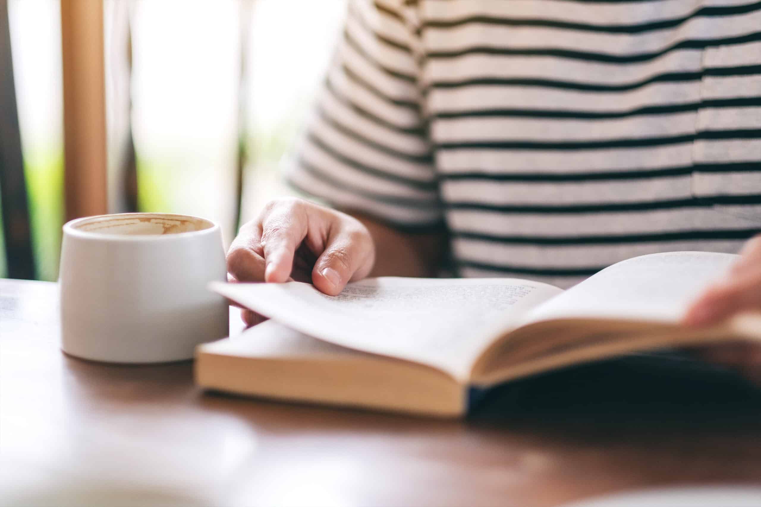 Torso of a person reading an open book with a cup of coffee