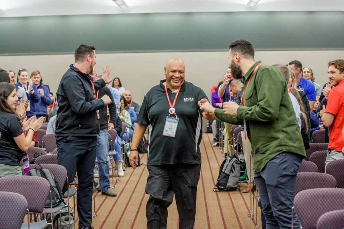 Person walks down an aisle smiling with people surrounding them clapping.