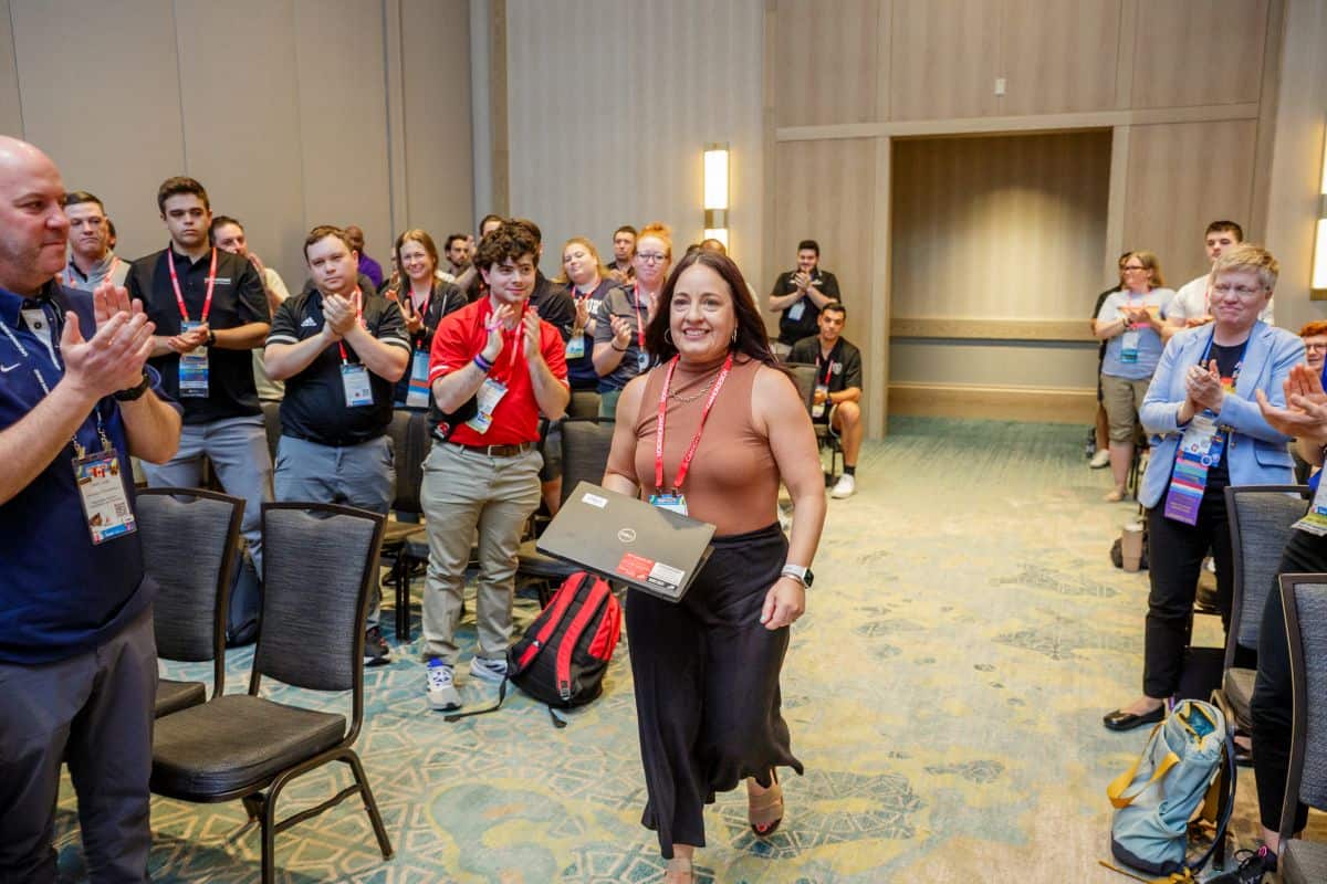 Person walking to the front of a room with people standing and clapping around them.